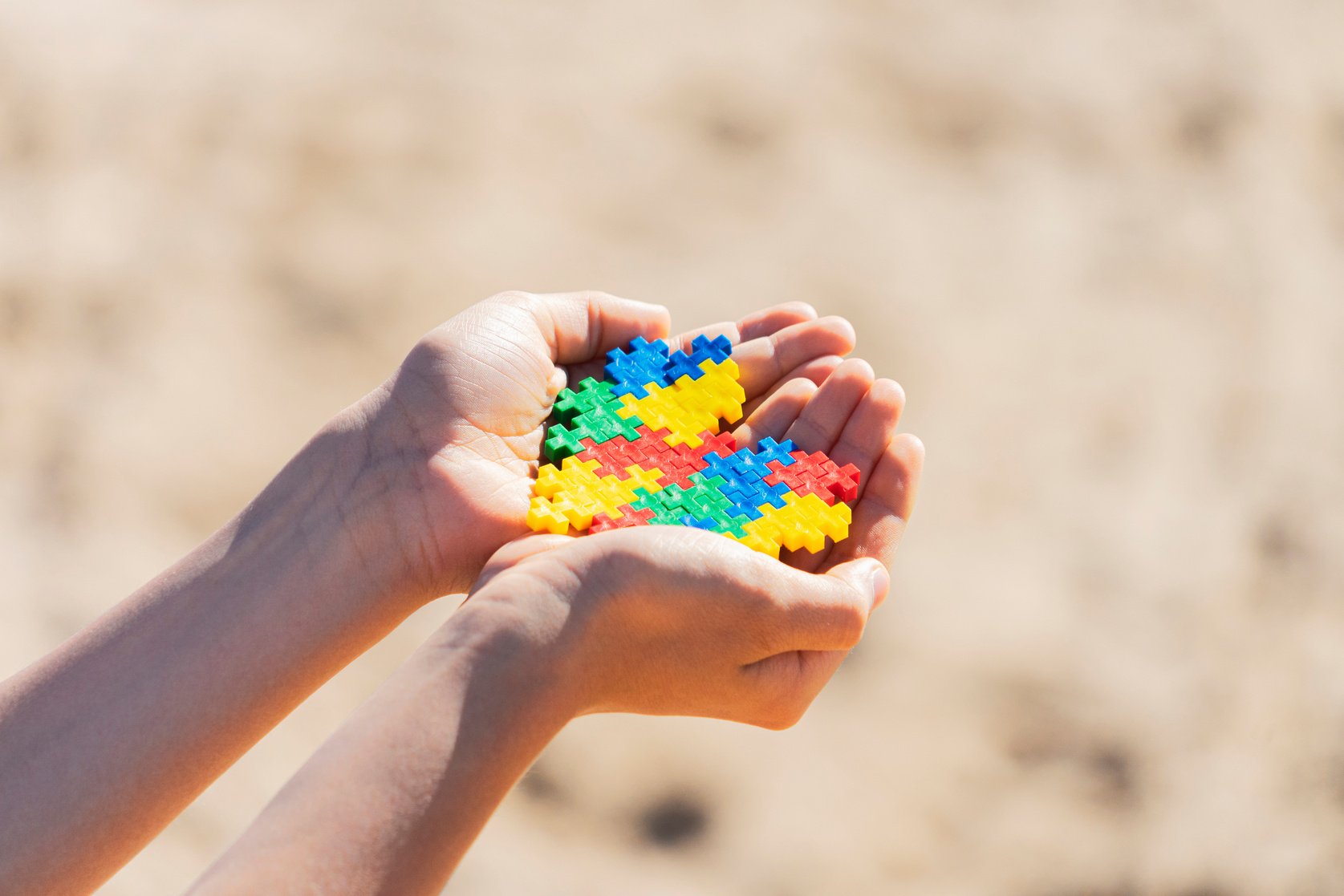 Child's Hands Holding a Multicolored Puzzle Heart Outdoors